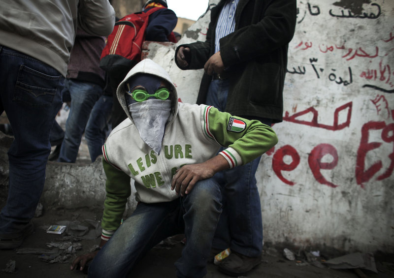 A protester wearing swimming goggles crouches as riot police fire tear gas Tuesday near Tahrir Square. The military said it would move up presidential elections to early 2012.
