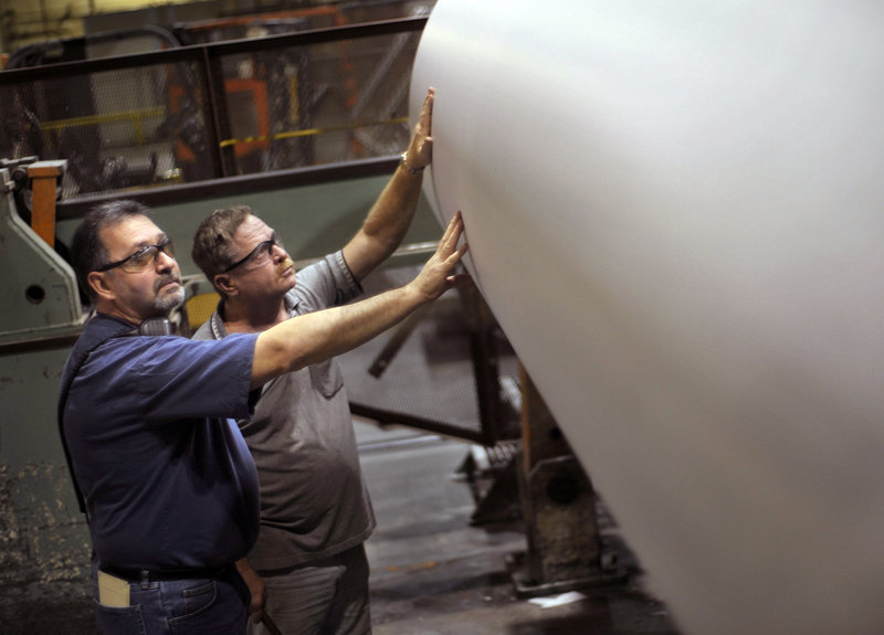 Rick Nicholson, left, and Louis Ouellette inspect a roll of paper on the operation floor of the Great Northern Paper Co. mill in East Millinocket this week. Idled for months, the mill is back in operation, making newsprint and employing more than 200 paper-makers. The prospect of continued investment has provided a glimmer of hope for workers in a region that’s rich in natural resources but short on jobs.
