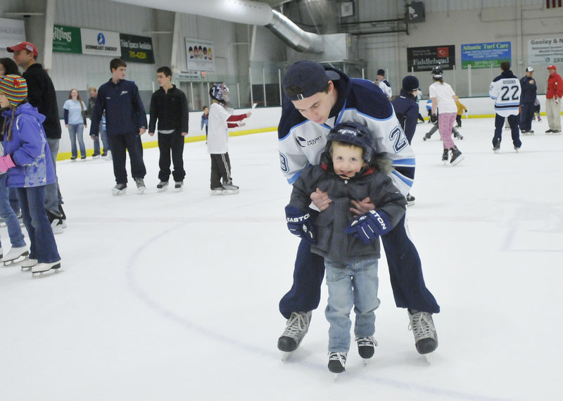 Kieran MacDonald, a 3-year-old from Levant, gets a little help skating from Connor Leen of the University of Maine during public skating time.