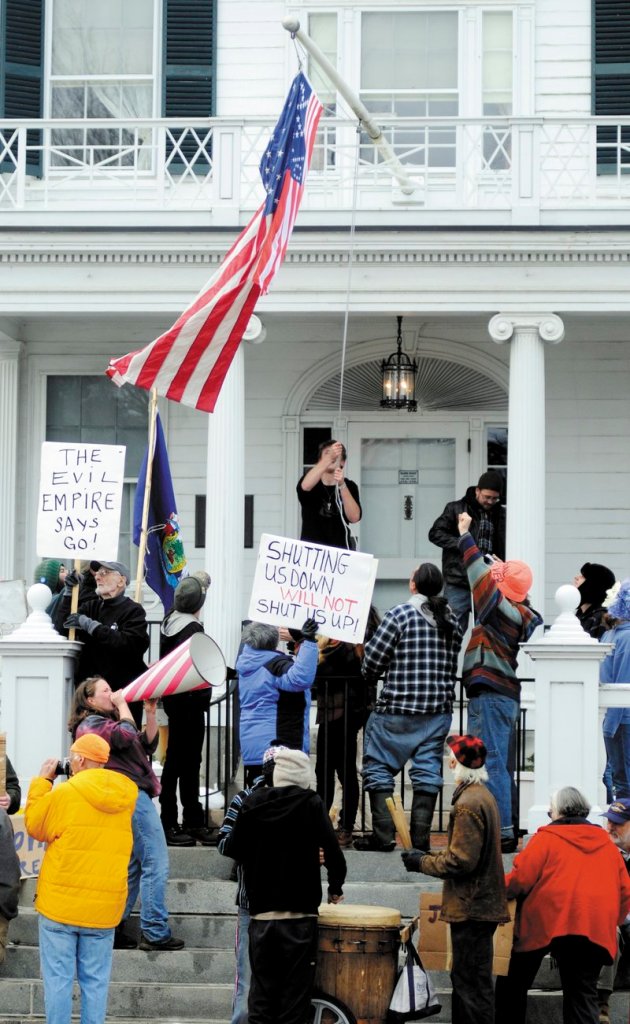 Occupy Augusta protesters hoist a flag embroidered with 99%, as well as an American flag, Sunday at the Blaine House.
