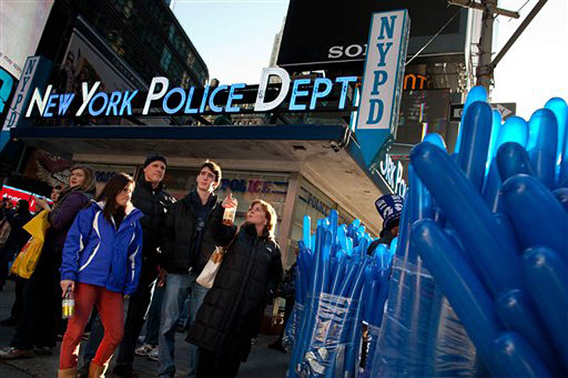 Bundles of balloons and curious pedestrians wait at a crosswalk outside the Times Square police station as city police officials begin ramping up security before Saturday's New Years Eve celebrations, Friday, Dec. 30, 2011, in New York. (AP Photo/John Minchillo)