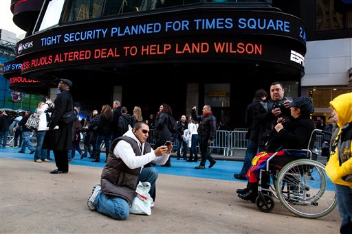 A news ticker reports planned tightening of security in Times Square while a tourist takes a snapshot before Saturday's New Years Eve celebrations, Friday, Dec. 30, 2011, in New York. (AP Photo/John Minchillo)