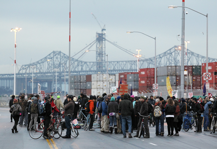With the San Francisco-Oakland Bay Bridge in the background Occupy protesters block one of the entrances to the Port of Oakland today, in Oakland, Calif.