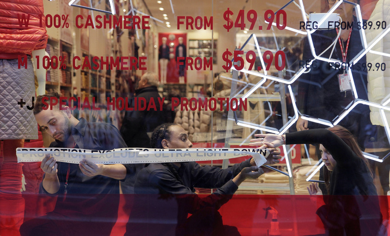 Employees of Uniqlo paste promotional information in a window of the retailer’s New York City store. Americans have become increasingly blase about bargains this holiday season.