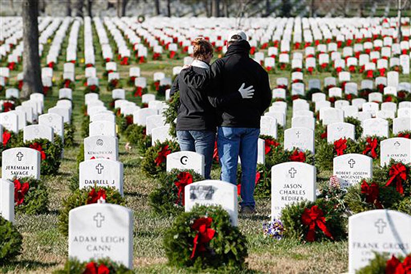 Volunteers pause over the grave of a fallen soldier after laying a holiday wreath during Wreaths Across America Day at Arlington Cemetery today.