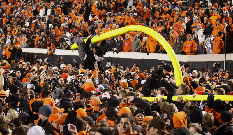 A fan hangs from a goal post after Oklahoma State's 44-10 football win over the University of Oklahoma in Stillwater, Okla., on Saturday, as thousands of fans flooded the field.