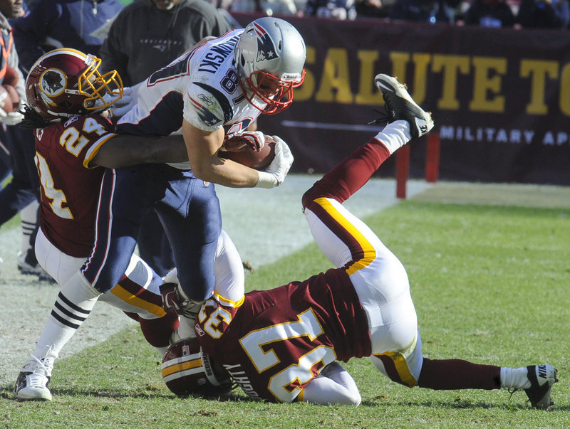 Rob Gronkowski fights for extra yards while trying to break tackles by Washington’s DeJon Gomes, 24, and Reed Doughty in Sunday’s game at Landover, Md. Gronkowski scored two TDs to set the single-season record for TD catches by a tight end.