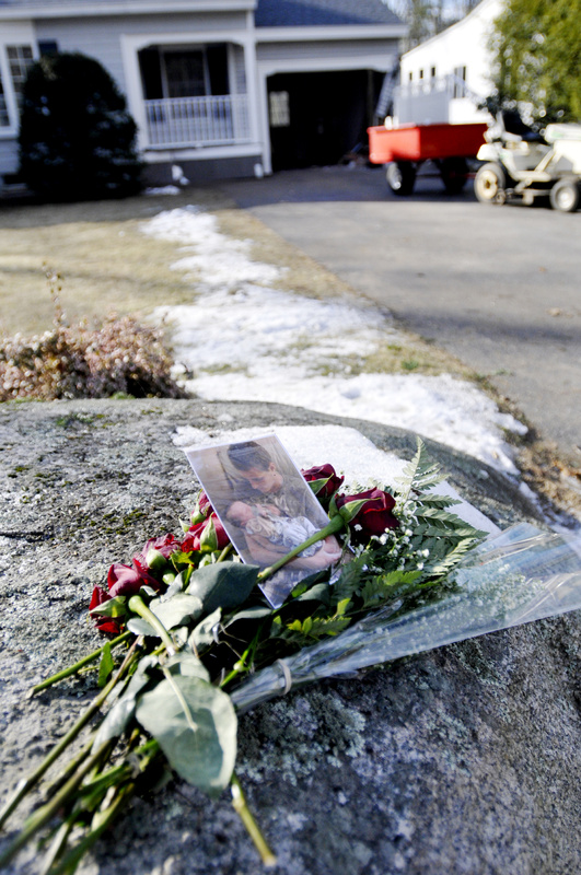 Flowers and a photograph lie on a rock at the foot of the driveway.