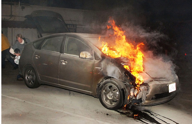 A car owner tries to retrieve possessions from his vehicle as it burns due to arson early Monday in a parking lot in Los Angeles. Eleven more suspected arson fires burned early Monday in the city.