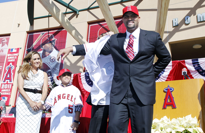 Los Angeles Angels' Albert Pujols puts on his new jersey as his wife Deidre Pujols, left, and his son Alberto Pujols Jr. look on during a baseball news conference in Anaheim on Dec. 12, 2011.