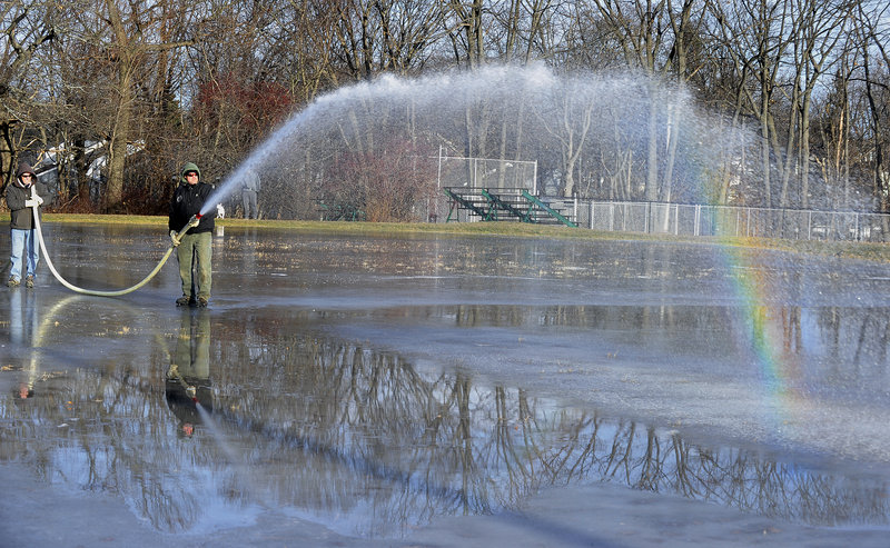 Supervisor Henry Fontaine holds the hose steady while Dave Smith, a city parks technician, directs the spray as they flood a skating area Wednesday at Payson Park in Portland. The rainbow was a bonus.