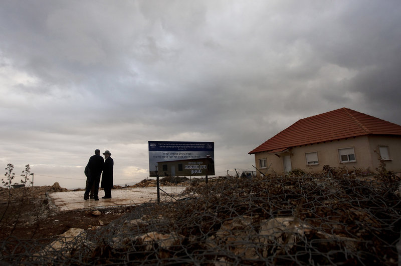 Settlers walk near the remaining foundation of a demolished house in the Jewish settlement of Migron earlier this week where a sign calls for its rebuilding. About 300 people live in Migron, the largest of over 100 unauthorized enclaves.