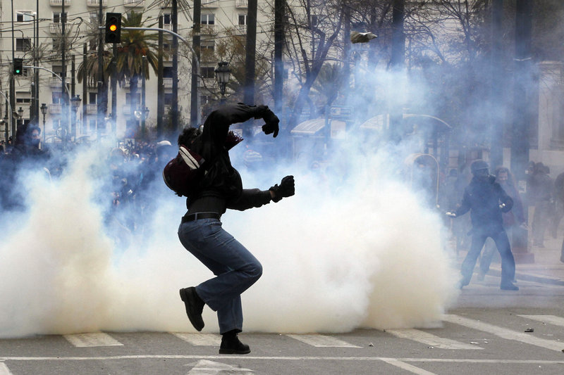 A protester throws a stone toward riot police in Athens on Friday as a cloud of tear gas envelops another at an anti-austerity demonstration.