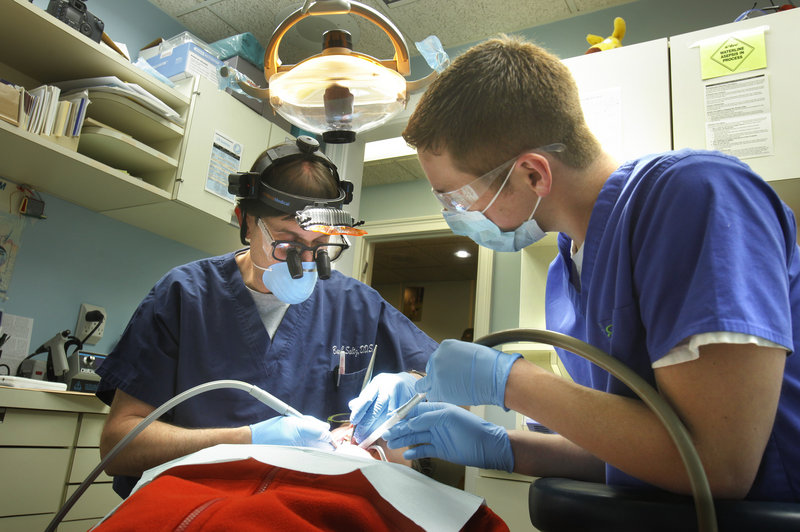 Dr. Barry Saltz, left, assisted by Tim Kilgo, works Monday with patient Danielle Romanoff in his Portland dentistry office. Saltz is pleased that UNE’s new dental school in Portland, which opens in the fall of 2013, will send students on rotations around the state to provide care.