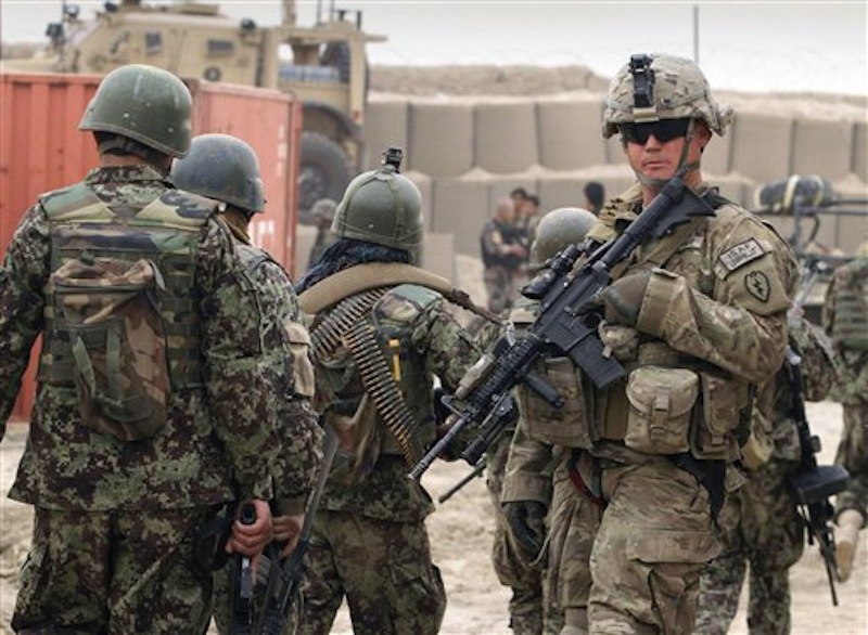 Afghan soldiers, left, walk past a U.S. Army soldier outside of a military base in Panjwai, Kandahar province south of Kabul, Afghanistan on Sunday, March 11, 2012. Afghan President Hamid Karzai says a U.S. service member has killed more than a dozen people in a shooting including nine children and three women. Karzai called the attack Sunday "an assassination" and demanded an explanation from the United States. He says several people were also wounded in the attack on two villages near a U.S. base in the southern province of Kandahar. (AP Photo/Allauddin Khan)