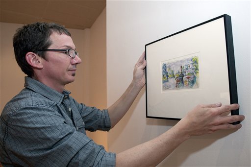 Director of DAAP Galleries at the University of Cincinnati, Aaron Cowan hangs a piece of art by art forger Mark A. Landis.