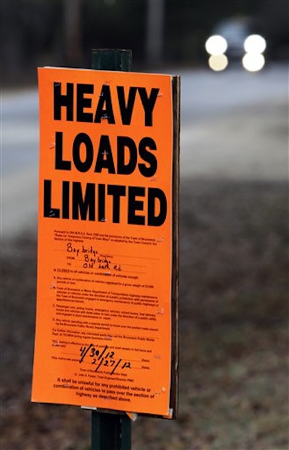 In this Wednesday, March 14, 2012 photo, a vehicle approaches a sign posted along a road prohibiting heavy trucks to use it in Brunswick, Maine. Hundreds of miles of roads are posted as the spring thaw comes early to northern New England. (AP Photo/Pat Wellenbach)
