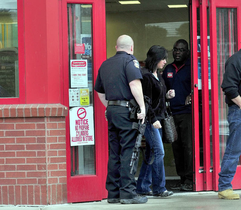 EXIT: Customers leave CVS Pharmacy on Kennedy Memorial Drive in Waterville past heavily armed police officer Denis Picard and a store employee while other officers search inside the store after a reported robbery on Sunday.