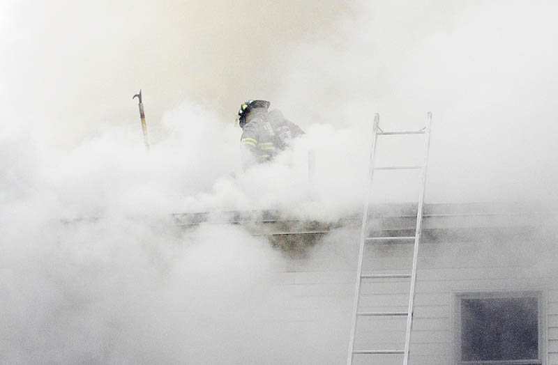 A firefighter cuts a hole in the roof to vent smoke from the blaze in a four-unit apartment building at 208 Hospital St. in Augusta on Friday. The Winthrop, Chelsea and Togus fire departments also responded to the fire that heavily damaged portions of the building.