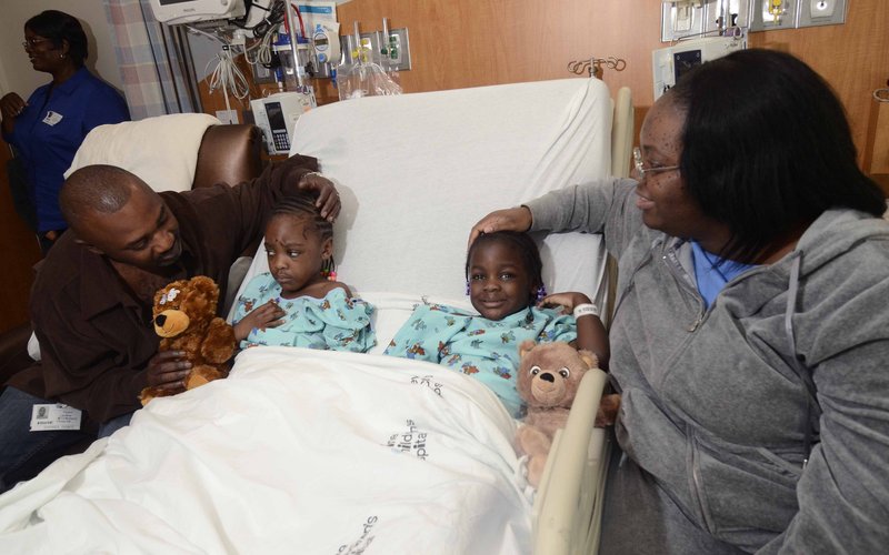 Sharing a hospital bed, Ayanna Stevens, 4, left, and her sister Amber Stevens, 3, recover after surviving a tornado at Levine Children’s Hospital, in Charlotte, N.C., as their parents, Tyrone and Latonya Stevens, sit by their side.