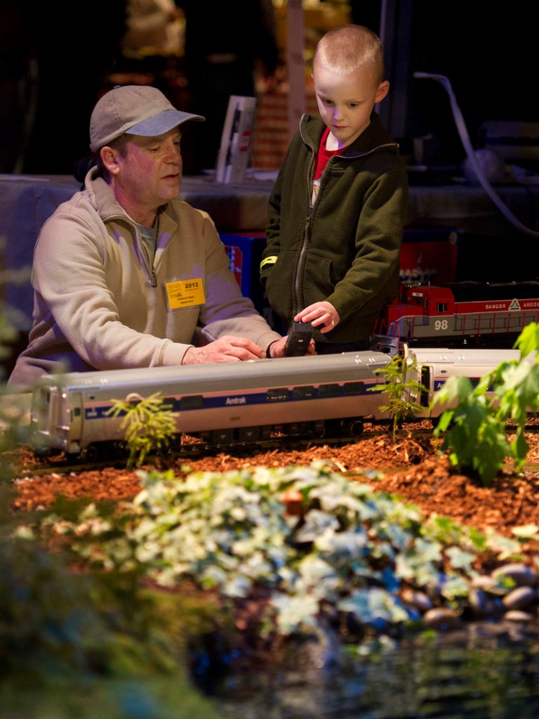 Chris Paquette of Robin's Nest Swimming Environments shows 6-year-old Jackson Fischer of Lisbon Falls how to operate a model train on Paquette's display during the opening of the Portland Flower Show on Wednesday.