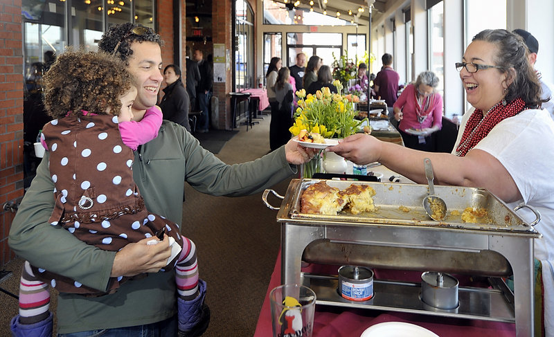 Andrew Tenenbaum of Portland, holding his daughter Harper, 3, gets a sample of the winning Creme Brulee French Toast served by Lisa Kostopoulos, owner of The Good Table restaurant in Cape Elizabeth, at the breakfast cook-off on Friday. She won by four votes.