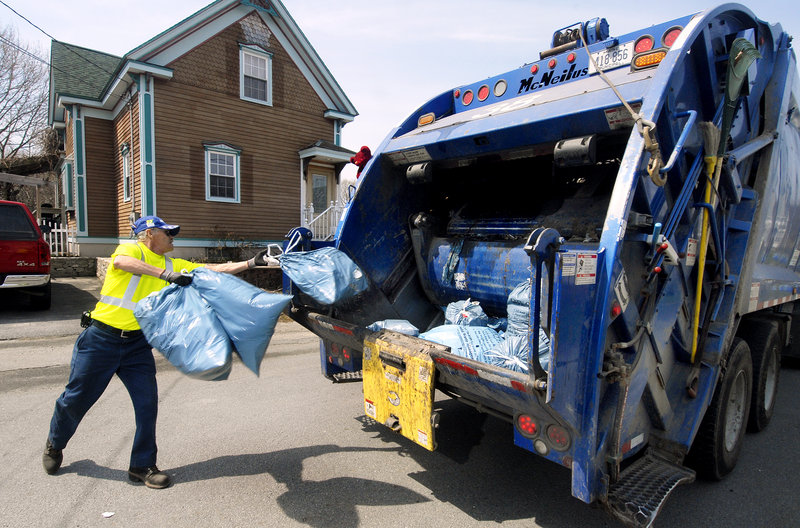 A worker tosses blue Portland trash bags into a garbage truck on Dalton Street.