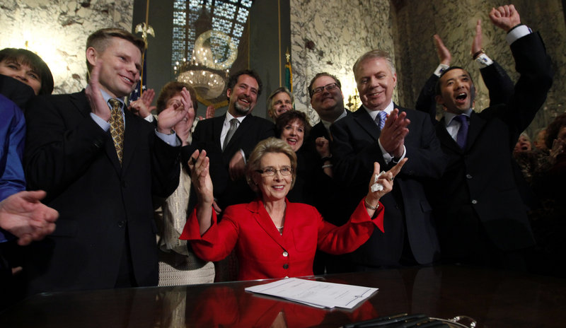 Washington state Gov. Christine Gregoire, seated, raises her arms as legislators and supporters cheer behind her after she signed into law a measure to legalize same-sex marriage.