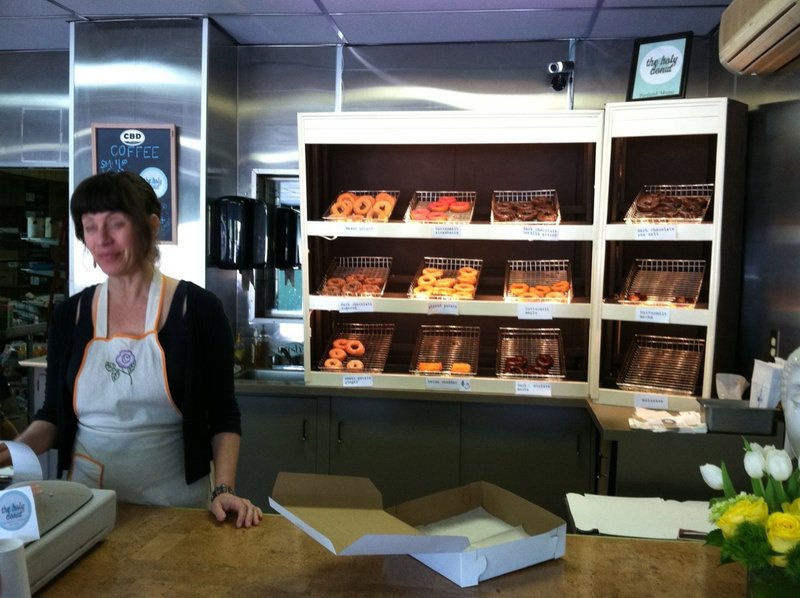Leslie Deane works the counter at the new Holy Donut, which opened last week in the former Terroni’s Market near Hadlock Field on Park Avenue in Portland. Below, an assorted dozen.