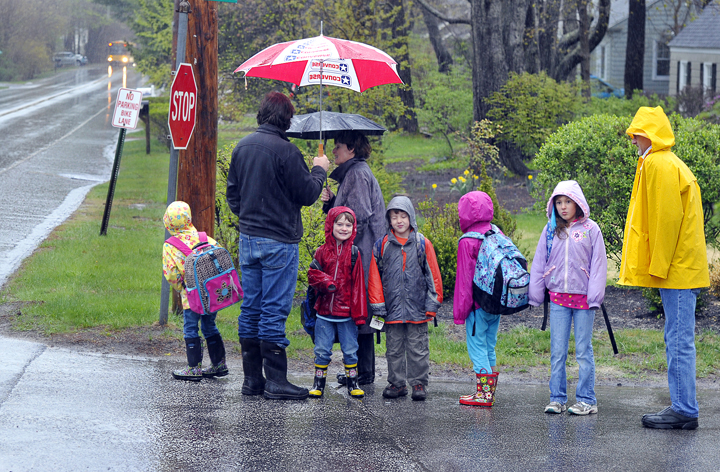 Three Mussel Cove families wait for the school bus in Falmouth as the rain falls heavily. The bus was about 15 minutes late and they were getting anxious. From left are parents Graham Haynes, Mary Smith and Mark Woodbury waiting with their children, who attend kindergarten through the third grade.