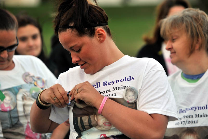VIGIL: Ashley Pouliot, center, pins a button with missing toddler Ayla Reynolds picture on to her Ayla Reynolds t-shirt before a vigil at the Church of God on Upper Main Street in Waterville Thursday.