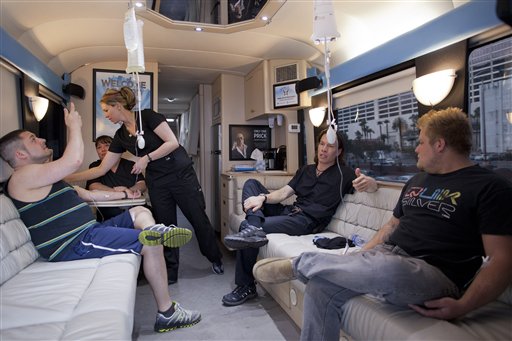 Bryan Dalia, left, of Caldwell, N.J. makes a photo of his IV bag while being treated on the Hangover Heaven bus by EMT Stacey Kreitlow, second from left, and Dr. Jason Burke, second from right, as another patient named Alex, right, looks on.
