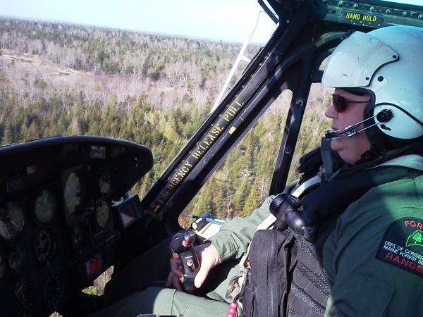 Ranger Chris Blackie pilots a Maine Forest Service helicopter over woods in Howland, where the search continues for Dean Levasseur, who has been missing since Saturday.