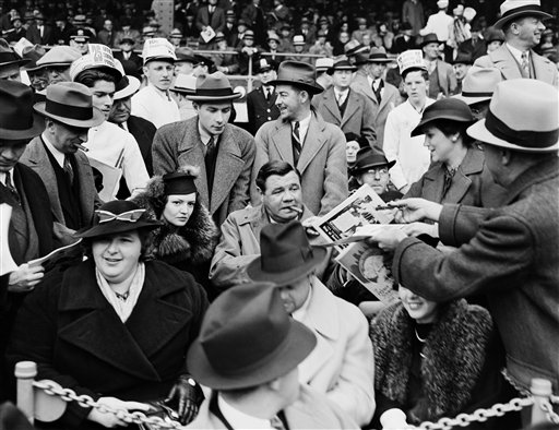 A man hands a program to baseball legend Babe Ruth, center, as he is joined by his second wife Clare, center left, and singer Kate Smith, front left, in the grandstand during Game 1 of the 1936 World Series at the Polo Grounds in New York. The photo is one of those posted online by the New York City Municipal Archives.