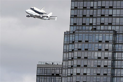 People watch from the balcony of a building as the space shuttle Enterprise, riding on the back of the NASA 747 Shuttle Carrier Aircraft, cruises over the Hudson River today.