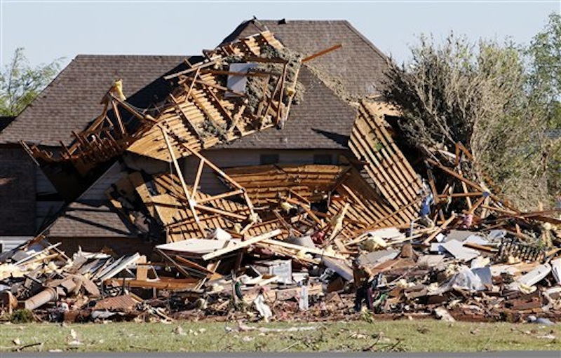 Sue Lord is dwarfed by the debris from her home, which is piled up on the neighbor's home, following a tornado in Woodward, Okla., Sunday, April 15, 2012. Lord was in the home when the tornado struck, but was not injured. (AP Photo/Sue Ogrocki)