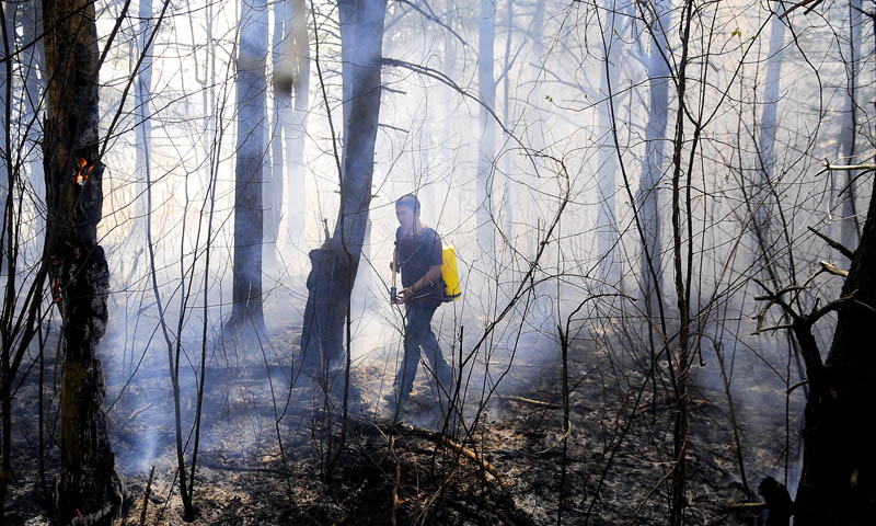 Staff photo by Andy Molloy BLAZE BUSTER: Caleb Trudeau searches for a hot spot Wednesday while extinguishing a brush fire along the Maine Turnpike in West Gardiner. Several fire companies responded to the blaze that covered the Turnpike with smoke.