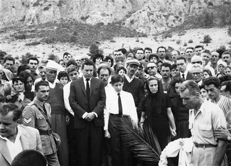 In this Sept. 13, 1962 file photo, Mike Wallace stands before his son Peter's grave as the casket is lowered at Kamari Village, Peloponnesus, Greece, after Peter Wallace fell to his death in a accident while climbing a steep mountain in Greece. Behind Wallace is his stepson Andrew, and next to him is his son, Chris, 14, with his mother, Norma Leonard, now Mrs. Bill Leonard, and Mrs. Lorraine Wallace. Wallace, the dogged, merciless reporter and interviewer who took on politicians, celebrities and other public figures in a 60-year career highlighted by the on-air confrontations that helped make "60 Minutes" the most successful primetime television news program ever, has died. He was 93. (AP Photo)