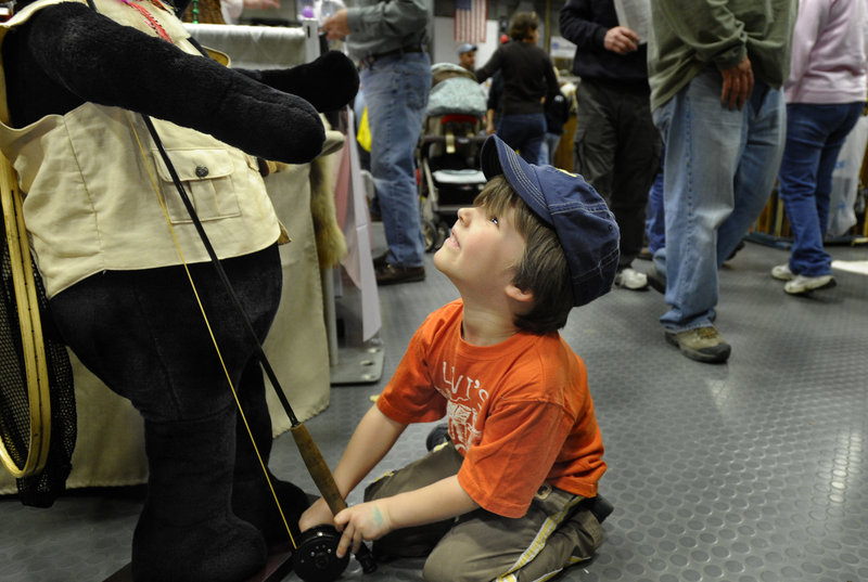 Oblivious to the hundreds of people milling around the floor of the Augusta Civic Center, Embden Nelson, 4, of Canaan, enjoys playing with a fishing rod in the hands of “Birdox the Bear” at the Maine Sportsman’s Show on Saturday.