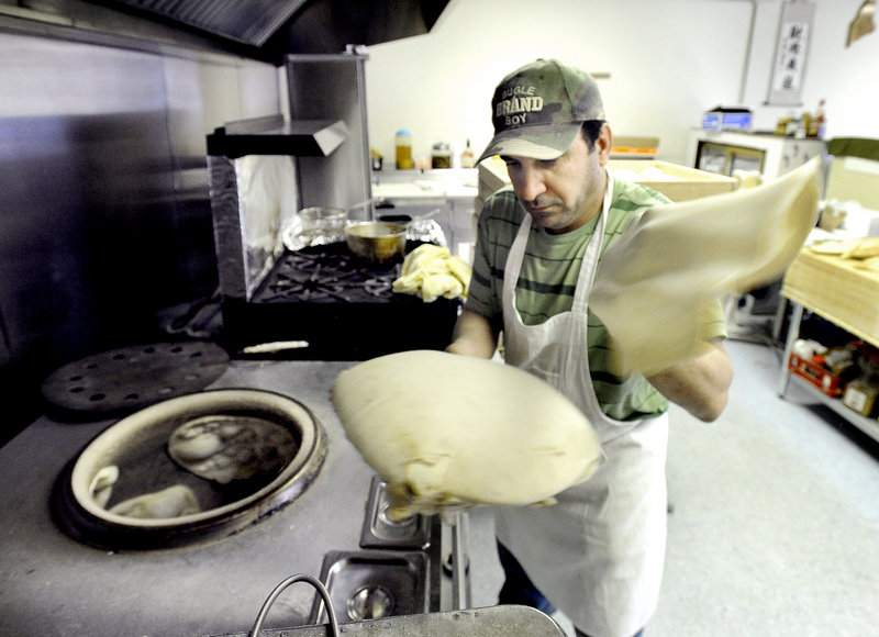 Audai Naser shapes flatbread dough before placing it into the circular tandoor oven to his right.