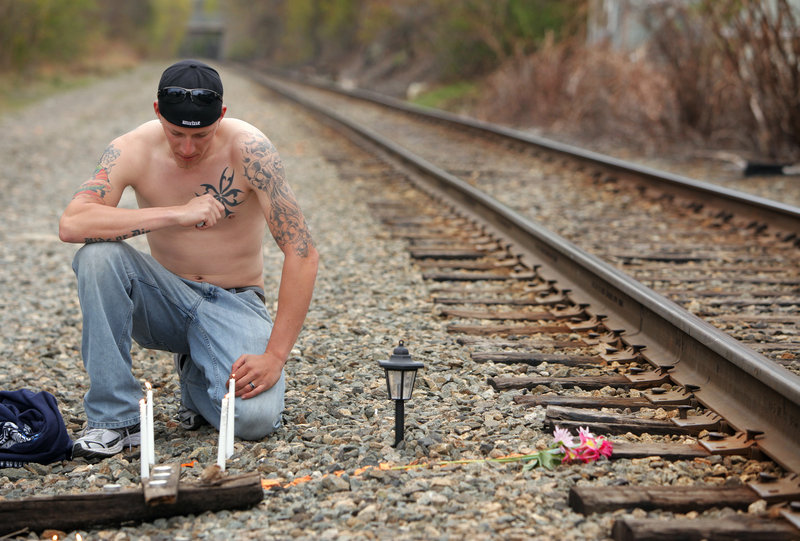 Matthew Ring tends candles during a vigil near the railroad tracks in Biddeford where 40-year-old Sean Page was killed by an Amtrak train on Monday. Ring removed his shirt to display his tattoos, all of which were done by his friend Page.