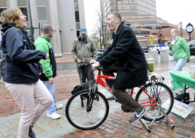 Julie Carey, a direct support professional with Creative Trails, encourages Ray Borg of Portland to pedal a bike rigged to power a blender for making “green” smoothies during the Urban Earth Day activities Sunday in Portland.