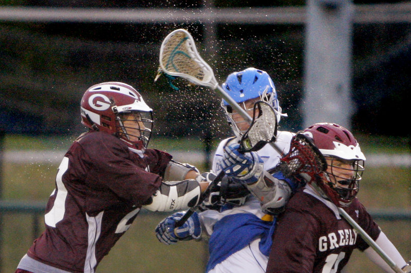 Water flies as Eric Story, left, and Christian Pisini, right, of Greely collide with Jack Coolen of Falmouth during Monday night’s game in the rain on Falmouth’s turf field.