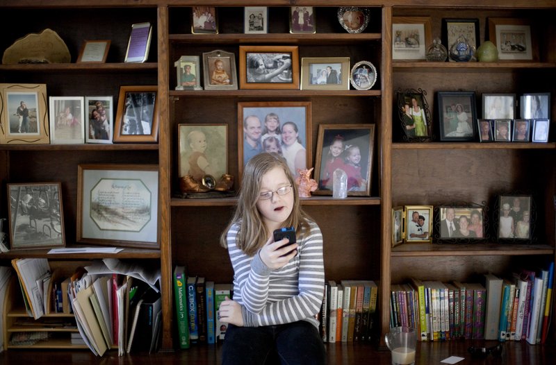 Alex Boston, 14, checks an email on a cellphone at home in Acworth, Ga. She has filed a libel lawsuit claiming two classmates humiliated her with a phony Facebook account.