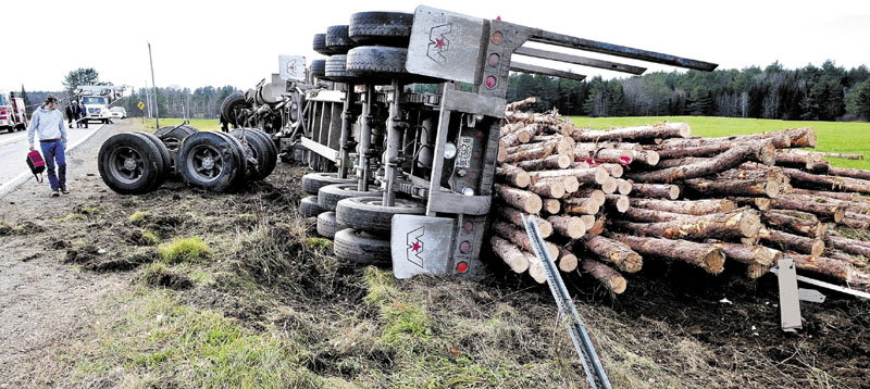 Driver Joseph Perrault, 30, of Norridgewock, walks past sheared-off axles and his pulp truck that rolled over and dumped logs near the intersection of Route 43 and the County Road in Madison in November 2011. Perrault escaped without injuries.