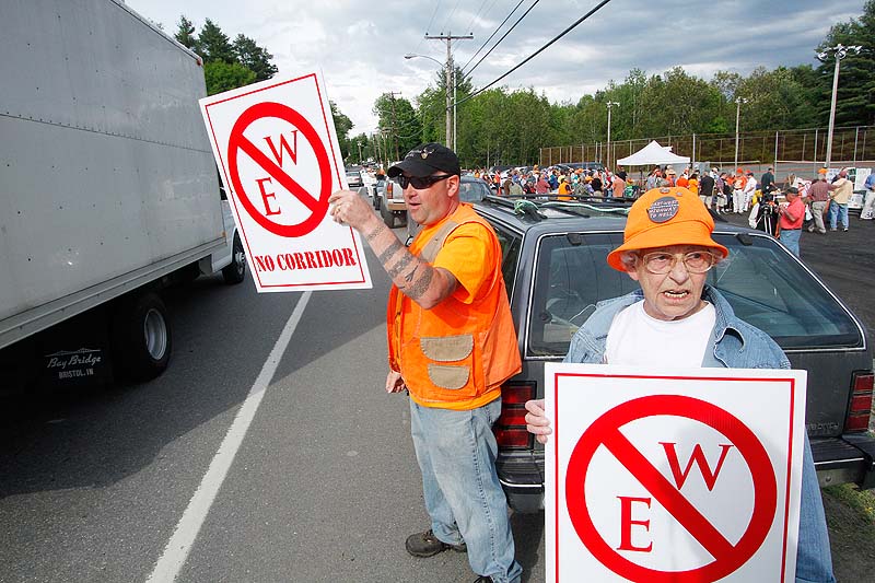 Rob Borden and Erla St. Pierre, both of Wellington, display signs in protest before a public meeting in Dover-Foxcroft concerning the proposed highway.