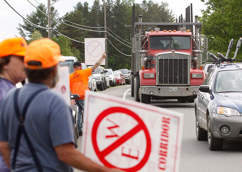 Protesters hold up signs up toward oncoming traffic before a public meeting in Dover-Foxcroft concerning the proposed East-West Highway.