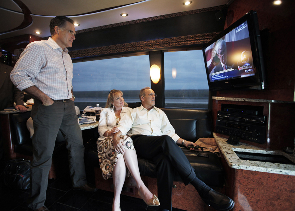 In this Jan. 29, 2012, photo, Republican presidential candidate Gov. Mitt Romney, left, watches Republican presidential candidate Newt Gingrich on television as he rides his Florida campaign bus with his brother Scott, and sister-in-law Sheri, to Hialeah, Fla.
