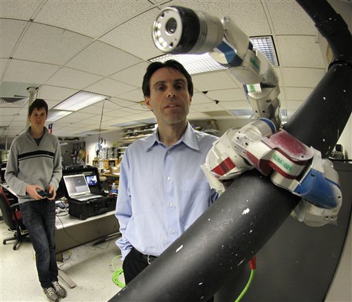 Carnegie Mellon University Professor Howie Choset, right, watches a robot as staff researcher Florinan Enner uses a controller to demonstrate how it climbs up a tubular armature at their lab on campus in Pittsburgh.