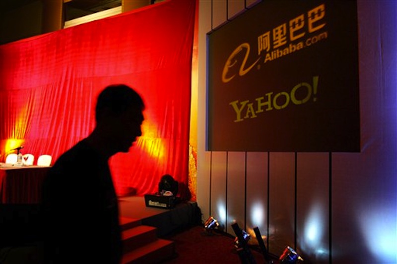 In this Aug. 11, 2005, file photo, a man walks past a screen displaying the Yahoo and Ali Baba.com logos before a joint news conference by the companies at the China World hotel in Beijing. Yahoo announced that it has agreed to sell half of its 40 percent stake in Chinese e-commerce company Alibaba for about $7.1 billion. The deal will see Alibaba Group buying back the stake from Yahoo Inc. for $6.3 billion cash and up to $800 million of Alibaba preference shares. (AP Photo/Elizabeth Dalziel, File)
